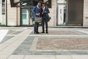 Two friends of black African American businessman in suits outdoors in a city block. Friendship and business partnership