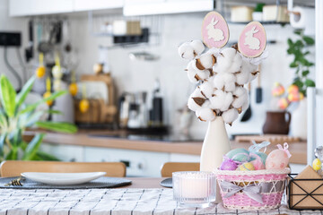 Easter decoration of colorful eggs in a basket and a rabbit on the kitchen table in a rustic style. Festive interior of a country house