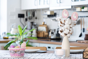 Easter decoration of colorful eggs in a basket and a rabbit on the kitchen table in a rustic style. Festive interior of a country house