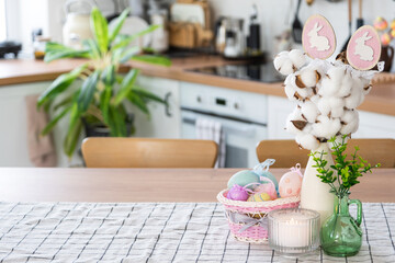 Fototapeta na wymiar Easter decoration of colorful eggs in a basket and a rabbit on the kitchen table in a rustic style. Festive interior of a country house