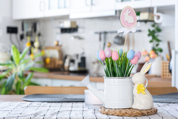 Easter decoration of colorful eggs in a basket and a rabbit on the kitchen table in a rustic style....