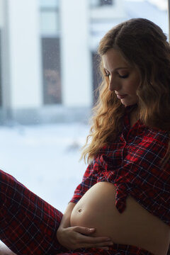 A pregnant woman in the living room with cup of tea near the window.