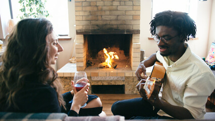 Young couple sit and hug with glass of wine in front of fireplace