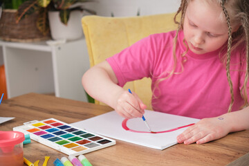 activities with a child concept, a cute girl with blond long hair draws a rainbow on paper