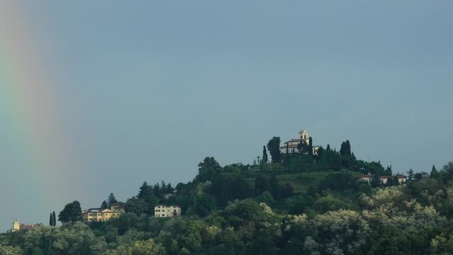 Beautiful colorful rainbow bridge. Green hill and gray clouds, full of rain in the background. Sanctuary church of Montevecchia.