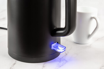 Electric kettle switch glows blue while turned on. Matte black kettle for heating water to boiling for tea and coffee. Modern class 1 electrical appliances for kitchen concept.