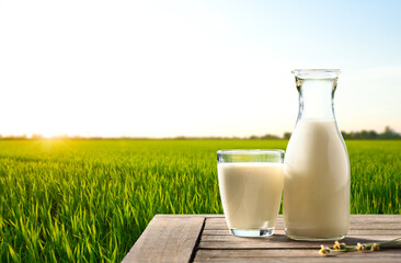 Fresh milk on wooden table with grass field and sunrise background.