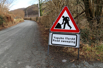 A Welsh bilingual triangular sign warning motorists that the road is being swept.