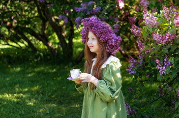 portrait of a girl with long red hair in a wreath of lilacs in the garden in spring