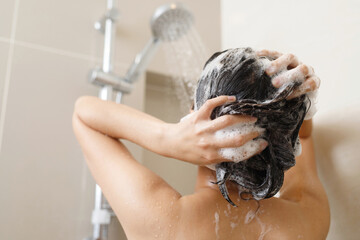 Woman taking shower and washing hair with shampoo in bathroom at home