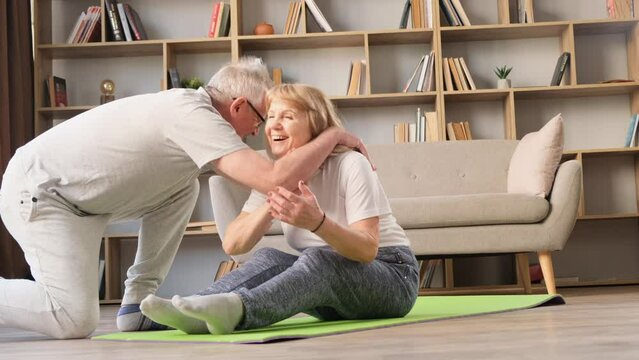 Senior couple doing sports at home, husband helping wife to do exercises. A happy couple