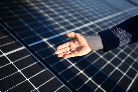 Rechte Hand eines Elektro Installateurs zeigt sparsame Fotovoltaik Solaranlage mit 10kW zur Sonnenstrom Erzeugung. PV Panels unscharf im Hintergrund. Stromrechnung senken.