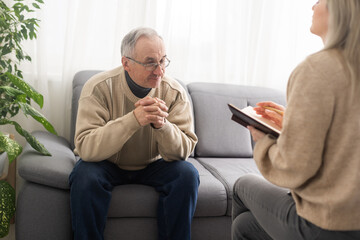 Senior man patient and young woman caregiver medical worker in uniform hold clipboard noting personal information talking listens client telling about health complaints, care support nursing concept