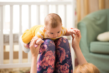 Young mother working out at home on a mat with baby. Interior of a cozy sunny nursery room. Woman...