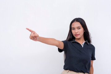 A pretty and young asian woman wearing a black polo shirt points to the left with her finger while looking at the camera. Endorsing a product or service. Isolated on a white background.