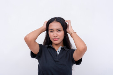 A pretty young Filipina intern in a black polo shirt with her hands on her scalp and jet black hair. Isolated on a white background.