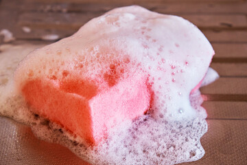 A pink kitchen foam sponge in detergent foam lies on a stainless steel sink. Close-up