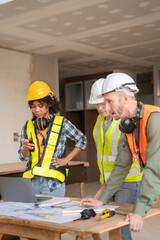 Architect colleagues mixed race working as a team discussing data working and tablet, laptop with on on architectural project at construction site at desk.