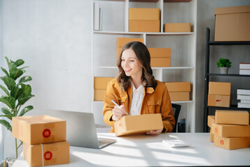 Obraz na płótnie Canvas Young business owner woman prepare parcel box and standing check online orders for deliver to customer on tablet, laptop Shopping Online concept..