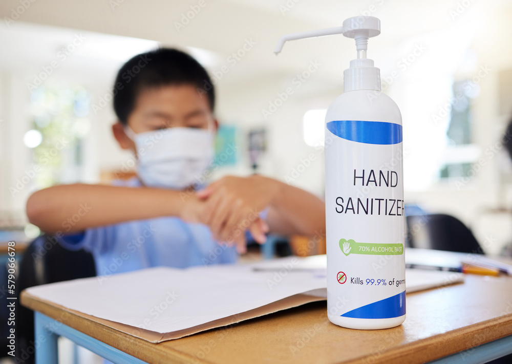 Sticker Boy rubbing hand sanitizer for hygiene, safety and protection against covid at school. Closeup bottle of alcohol gel on desk in classroom to clean, kill or prevent the spread of germs or coronavirus