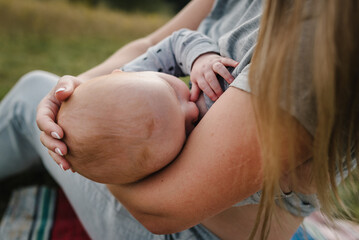 World Breastfeeding Week. Breastfeeding baby. Mother feeding breast newborn sits on grass in park....