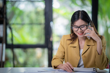 Happy businesswoman talking on mobile phone while analyzing weekly schedule in the office.