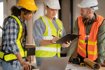 Architect colleagues mixed race working as a team discussing data working and tablet, laptop with on on architectural project at construction site at desk.