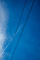 Fototapeta premium Crystal blue sky with clouds, high-voltage wires and airplane with trails high up