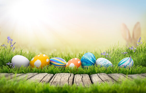 A collection of painted easter eggs celebrating a Happy Easter on a spring day with green grass meadow background with copy space and a rustic woodern bench to display products.