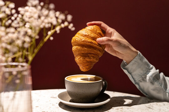 Close-up of a woman dipping a croissant in a cup of coffee