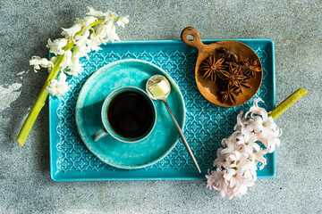 Overhead view of a cup of black coffee, a bowl of star anise and pink and white hyacinth flowers