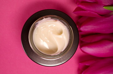 face cream in jar. close up. women's care concept. container with anti wrinkles cream on pink background with violet tulips