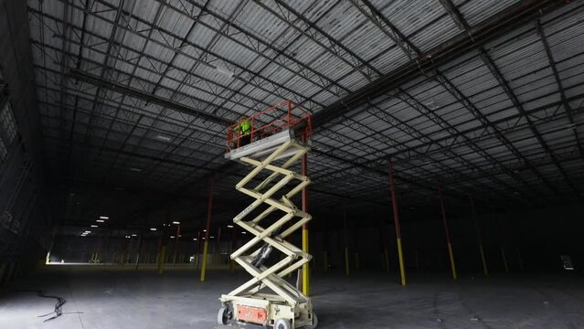 Man Operating A Scissor Lift In A Warehouse Under Construction.