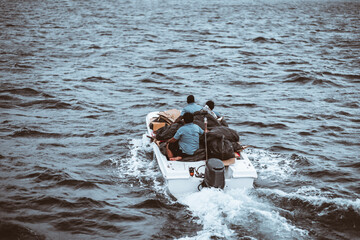A group of men in a white fisherman's boat is struggling, as the boat is packed with bags, and...