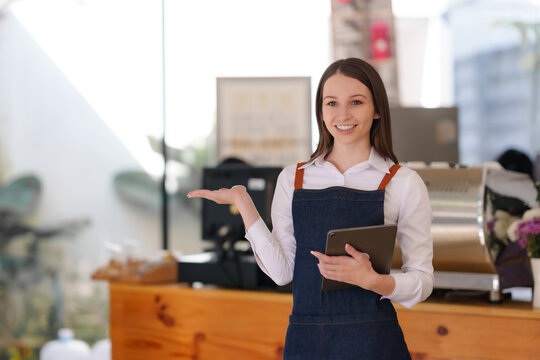 Young American woman small business owner in apron holding tablet at coffee shop. Looking at camera.