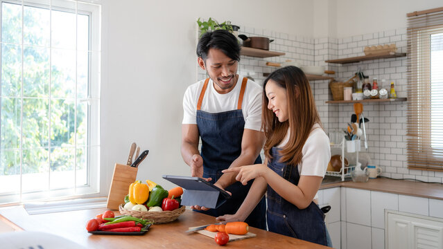 Happy Asian Couple Learning To Cook Through Tablet Together.