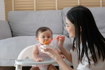 Young mother helping baby eating blend food on baby chair
