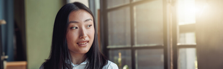 Asian businesswoman standing at office with phone and looking at window