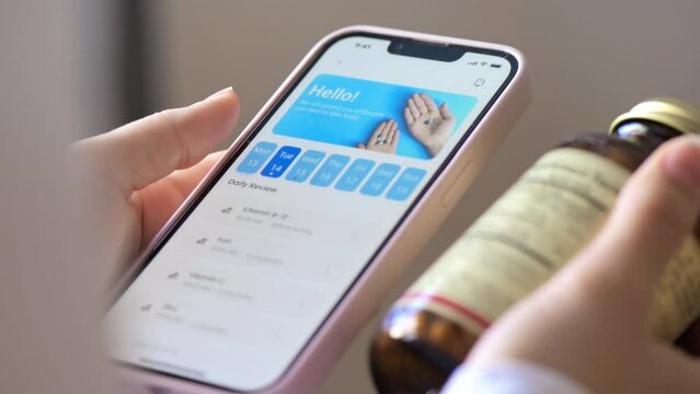 Close view of a person using smartphone with medication tracker app holding a jar of pills