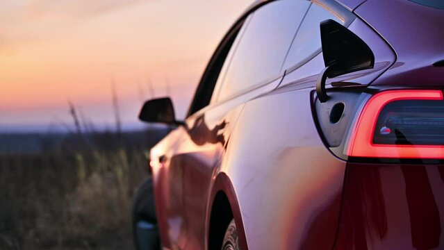 Close view of a parked red electric car opening charging port at sunset