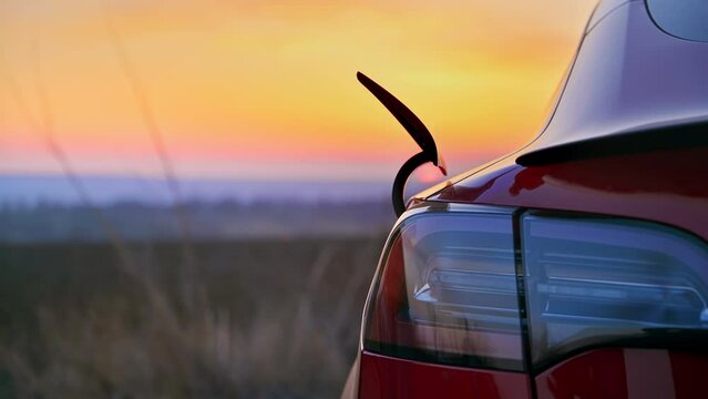 Close view of a man pulling out charging cable of a parked red electric car at sunset