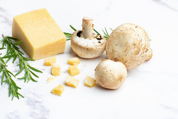 Champiñones junto a queso de rallar y unas ramitas de romero sobre un fondo de mármol con...