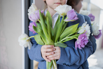unrecognizable child holds a bouquet of white and lilac tulips in front of him. Mother's day, international women's day, valentine's day. Flower surprise with love