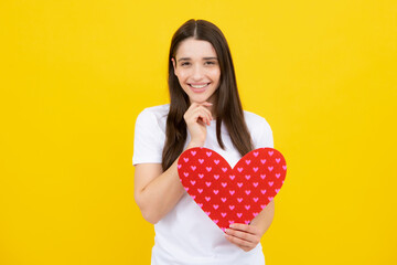 Girl feeling love. Beautiful young woman with heart in her hands. Attractive woman with paper heart over yellow background.