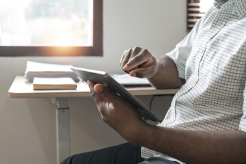 Fototapeta premium Smiling African American freelancer touching screen digital tablet while working in new project at home. Black businessman looking for information on Internet