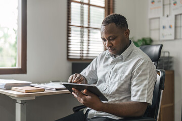 Smiling African American freelancer touching screen digital tablet while working in new project at home. Black businessman looking for information on Internet