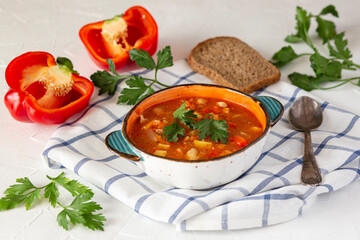 Hungarian goulash in a ceramic plate, bread, paprika, parsley on a white table