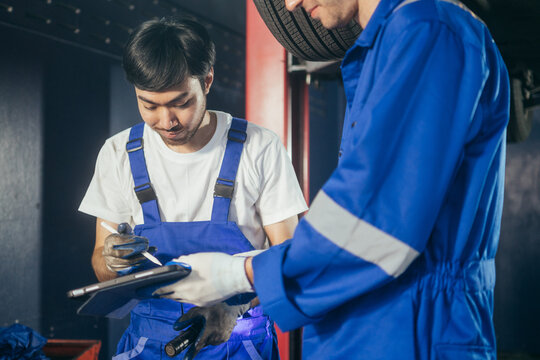 Asian mechanic worker signing on digital tablet for car maintenance service agreement at auto repair shop. After service and transportation career