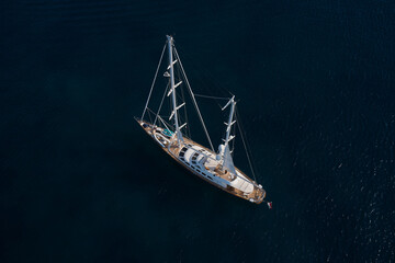 A large wooden yacht with masts without sails in the open sea on dark water, top view.