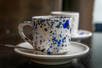 White coffee cup with blue spots on a saucer with a spoon on a wooden table